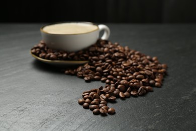 Photo of Aromatic coffee in cup and beans on black table, closeup