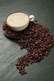 Photo of Aromatic coffee in cup and beans on black table, above view