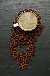 Photo of Aromatic coffee in cup and heart shaped of beans on black table, flat lay