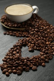 Photo of Aromatic coffee in cup and heart shaped of beans on black table, closeup