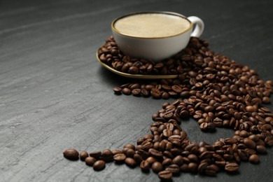 Photo of Aromatic coffee in cup and heart shaped of beans on black table, closeup. Space for text