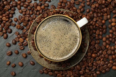 Photo of Aromatic coffee in cup and beans on black table, flat lay