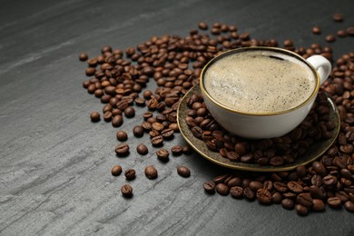 Photo of Aromatic coffee in cup and beans on black table, closeup. Space for text