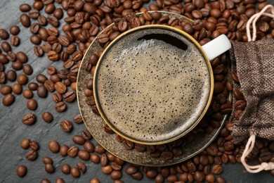 Photo of Aromatic coffee in cup and beans on black table, flat lay