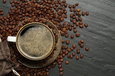 Photo of Aromatic coffee in cup and beans on black table, flat lay. Space for text