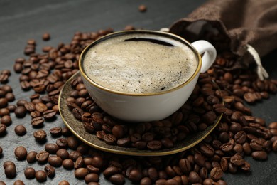 Photo of Aromatic coffee in cup and beans on black table, closeup