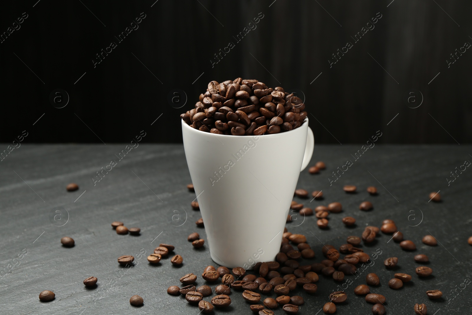 Aromatic coffee beans in cup on black table, closeup Photo of Aromatic coffee beans in cup on black table, closeup