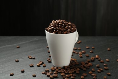 Photo of Aromatic coffee beans in cup on black table, closeup