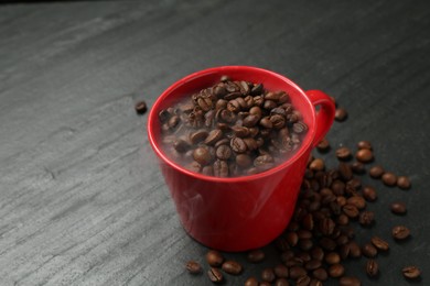 Photo of Aromatic coffee beans in cup on black table, closeup. Space for text