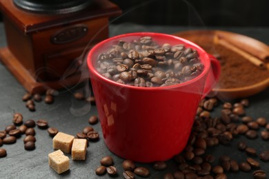 Photo of Aromatic coffee beans in cup, grinder and brown sugar on black table, closeup