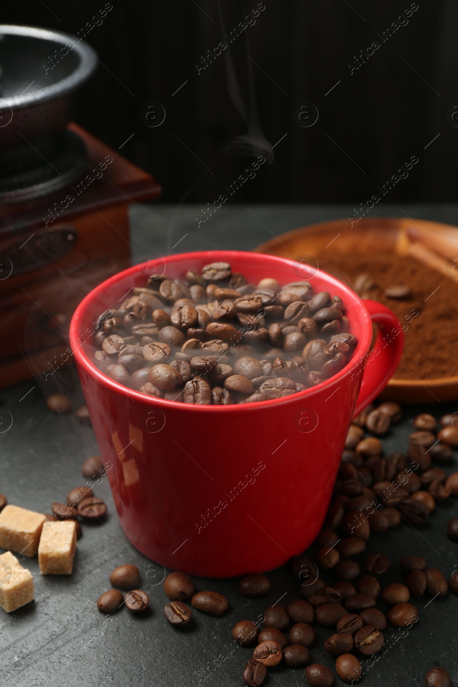 Aromatic coffee beans in cup, grinder and brown sugar on black table, closeup Photo of Aromatic coffee beans in cup, grinder and brown sugar on black table, closeup