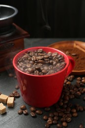 Photo of Aromatic coffee beans in cup, grinder and brown sugar on black table, closeup