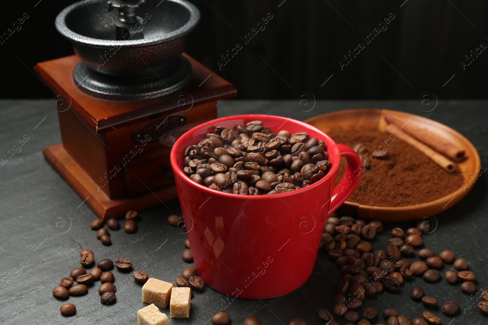 Aromatic coffee beans in cup, grinder and brown sugar on black table, closeup Photo of Aromatic coffee beans in cup, grinder and brown sugar on black table, closeup