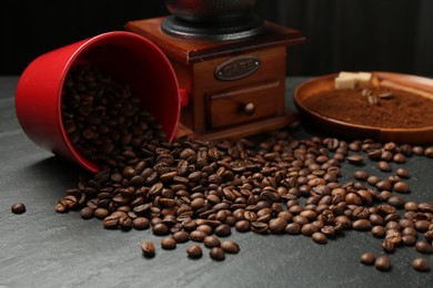 Photo of Aromatic coffee beans and grinder on black table, closeup