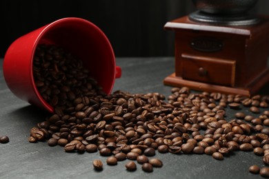 Photo of Aromatic coffee beans and grinder on black table, closeup