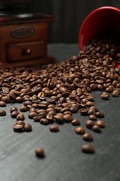 Photo of Aromatic coffee beans and grinder on black table, closeup