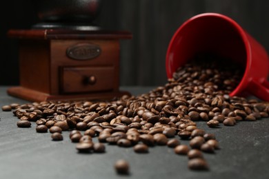 Photo of Aromatic coffee beans and grinder on black table, closeup