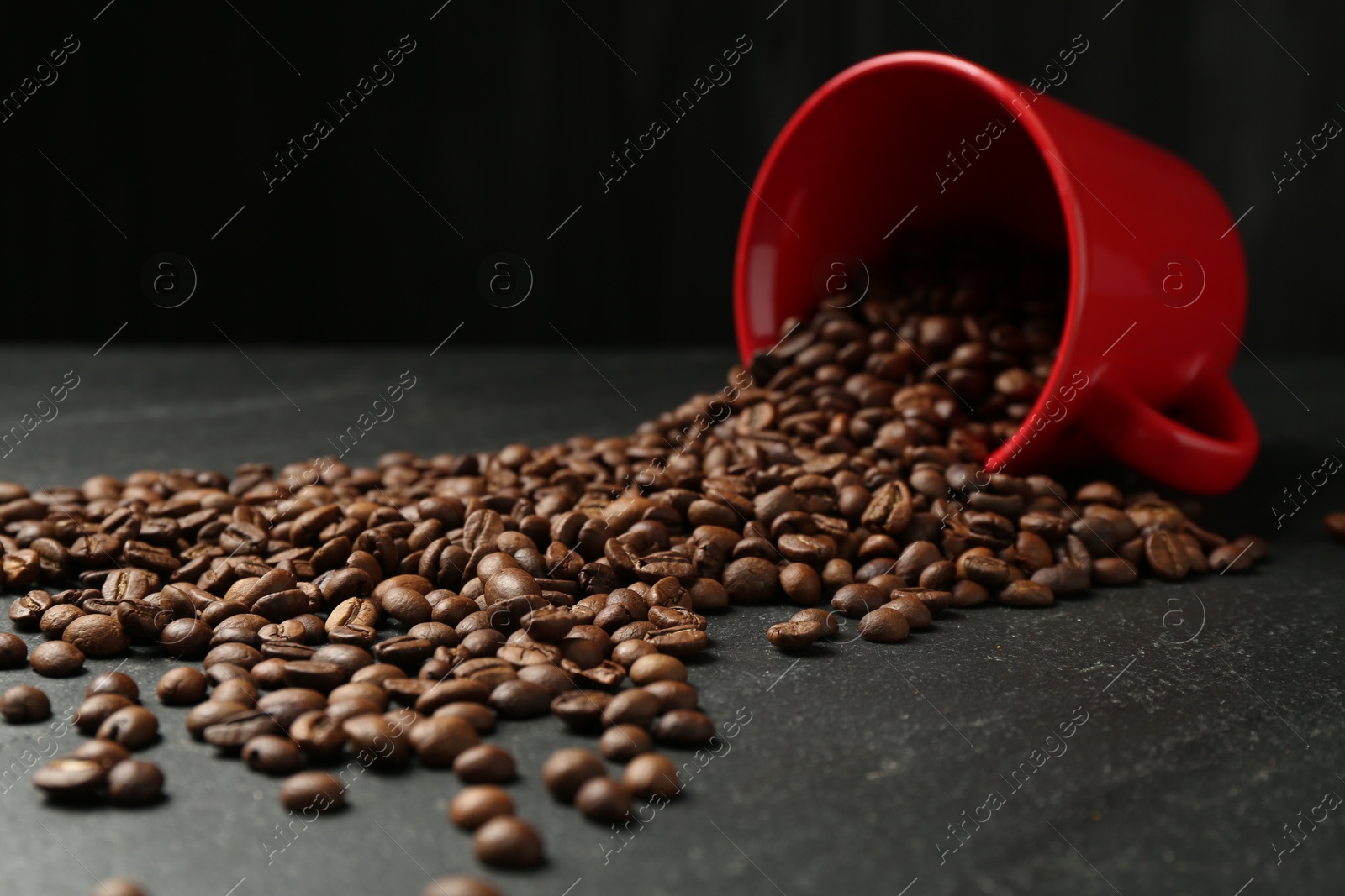 Aromatic coffee beans and overturned cup on black table, closeup Photo of Aromatic coffee beans and overturned cup on black table, closeup