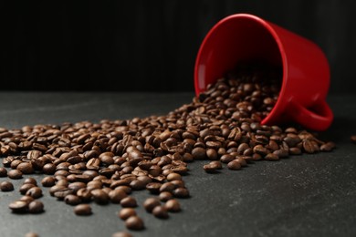 Photo of Aromatic coffee beans and overturned cup on black table, closeup