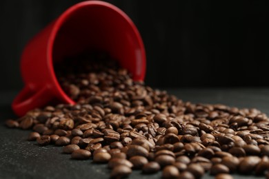 Photo of Aromatic coffee beans and overturned cup on black table, closeup
