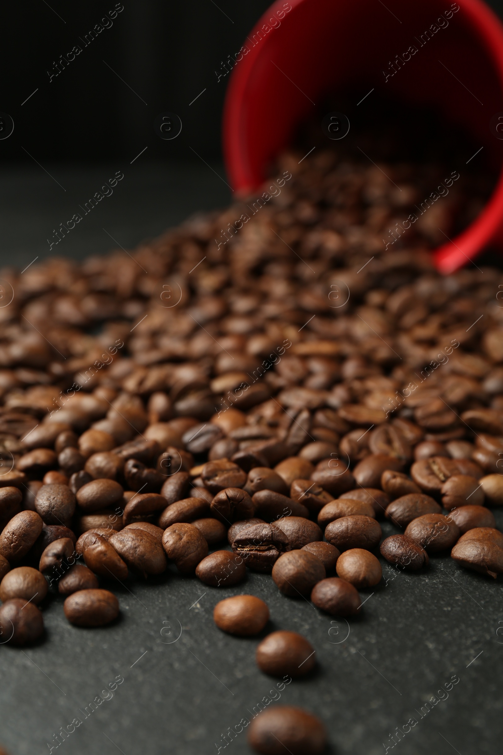 Aromatic coffee beans and overturned cup on black table, closeup Photo of Aromatic coffee beans and overturned cup on black table, closeup