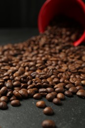 Photo of Aromatic coffee beans and overturned cup on black table, closeup