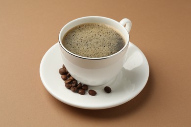 Photo of Aromatic coffee in cup and beans on beige background, closeup