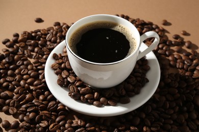 Photo of Aromatic coffee in cup and beans on beige background, closeup