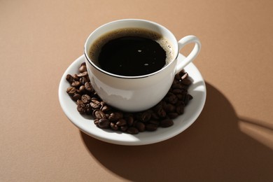 Photo of Aromatic coffee in cup and beans on beige background, closeup