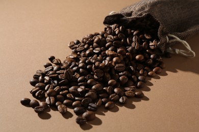 Photo of Aromatic coffee beans and sack on beige background, closeup