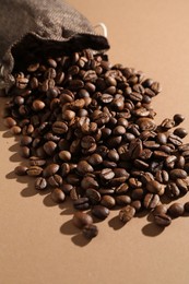Photo of Aromatic coffee beans and sack on beige background, closeup