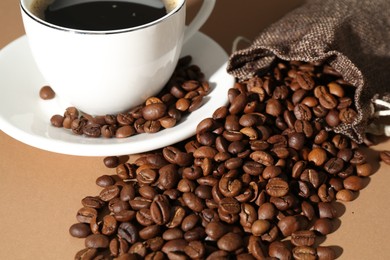 Photo of Aromatic coffee in cup and beans on beige background, closeup