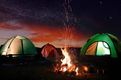 Image of Bonfire near camping tents outdoors at night