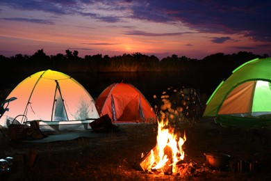 Image of Bonfire near camping tents outdoors at sunset