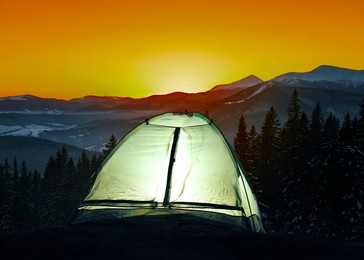 Image of Tent lit from inside in mountains at sunset. Camping season