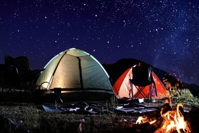 Image of Camping tents and bonfire in wilderness at night under starry sky