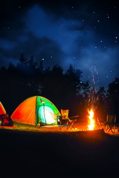 Image of Camping tents and bonfire in wilderness at night under starry sky