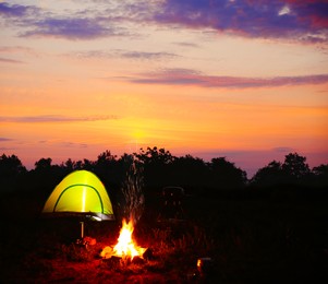 Image of Camping tent and bonfire in wilderness at sunset