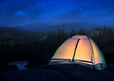 Image of Camping tent lit from inside in mountains at night under starry sky