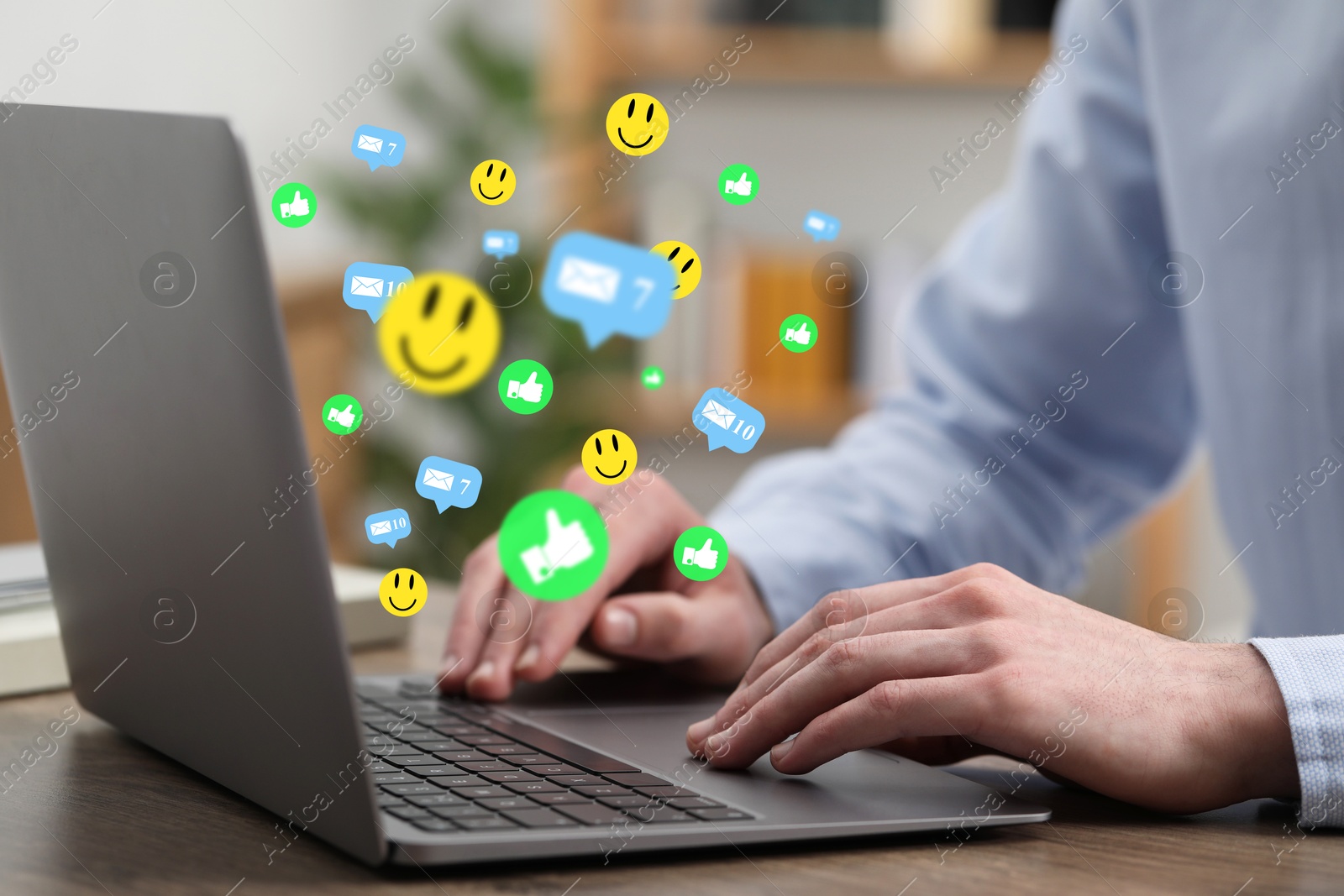 Man using laptop at table, closeup. Social media notifications (likes, messages and emojis) flying out of computer Image of Man using laptop at table, closeup. Social media notifications (likes, messages and emojis) flying out of computer