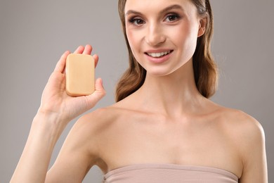 Photo of Smiling woman with soap bar on grey background, closeup