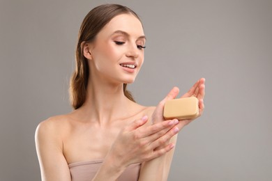 Photo of Smiling woman with soap bar on grey background