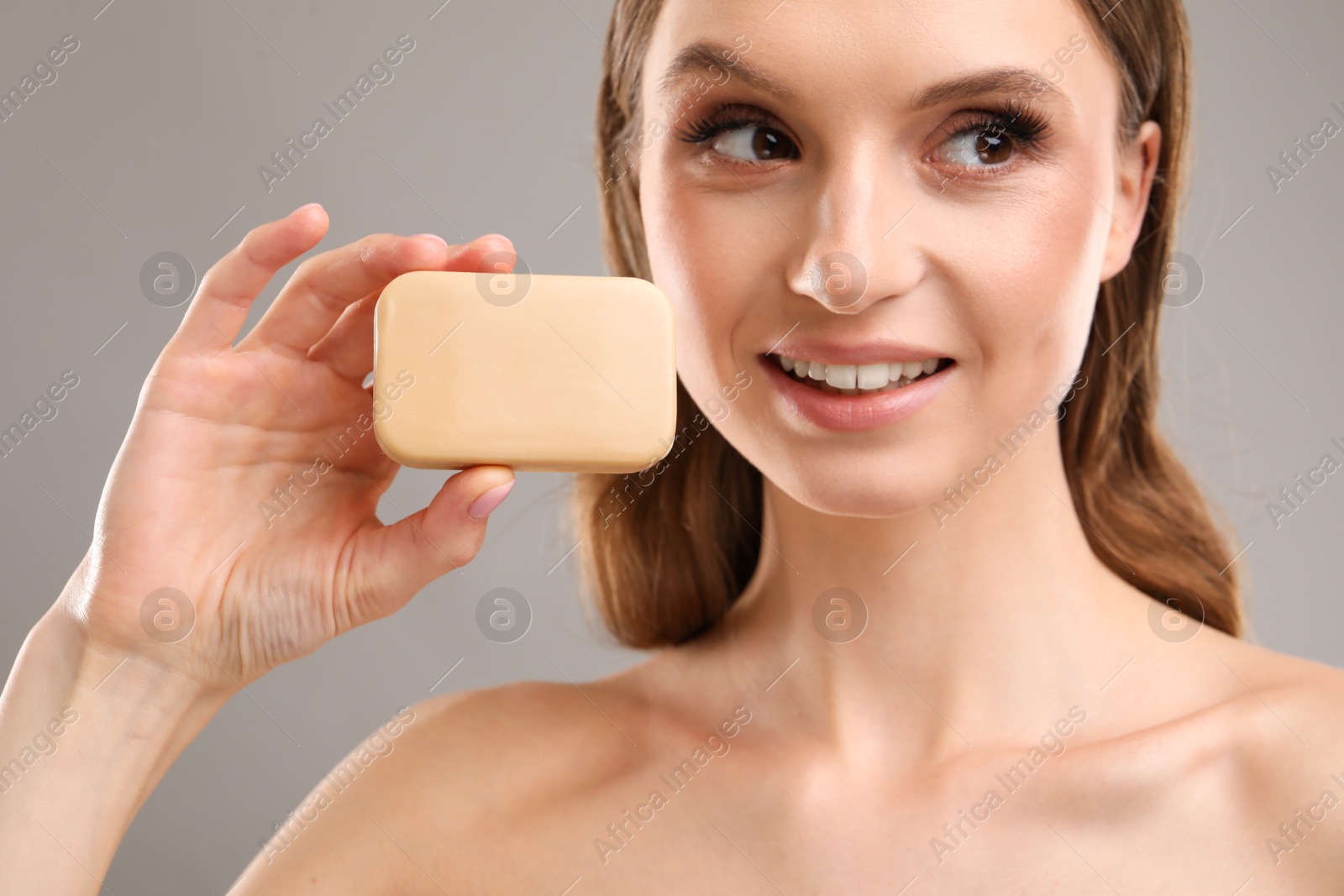 Smiling woman with soap bar on grey background, closeup Photo of Smiling woman with soap bar on grey background, closeup