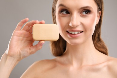 Photo of Smiling woman with soap bar on grey background, closeup