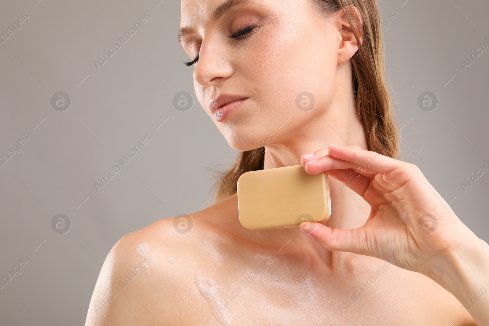 Beautiful woman with soap bar on grey background, closeup Photo of Beautiful woman with soap bar on grey background, closeup