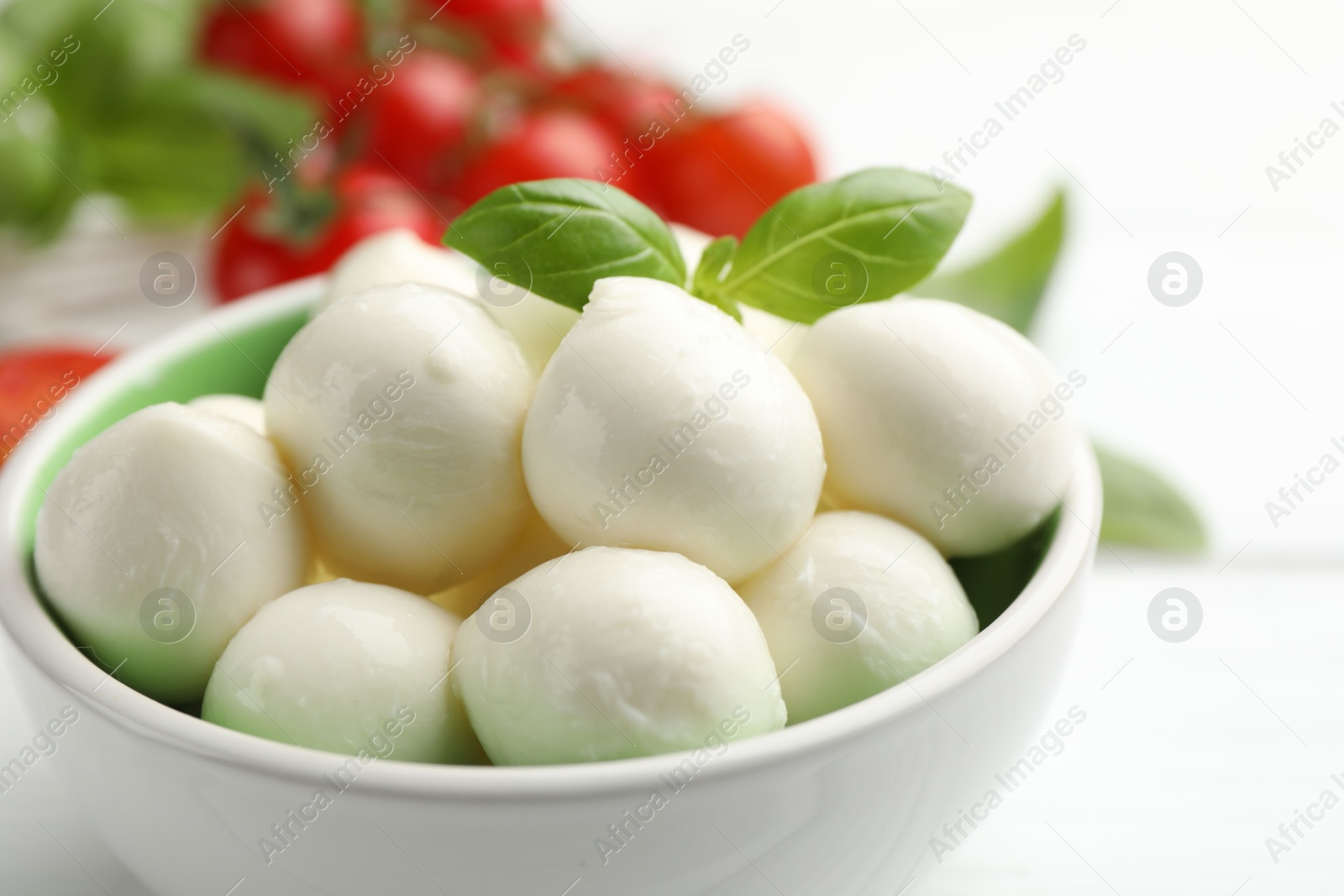 Tasty mozzarella cheese balls in bowl, basil and tomatoes on white table, closeup Photo of Tasty mozzarella cheese balls in bowl, basil and tomatoes on white table, closeup