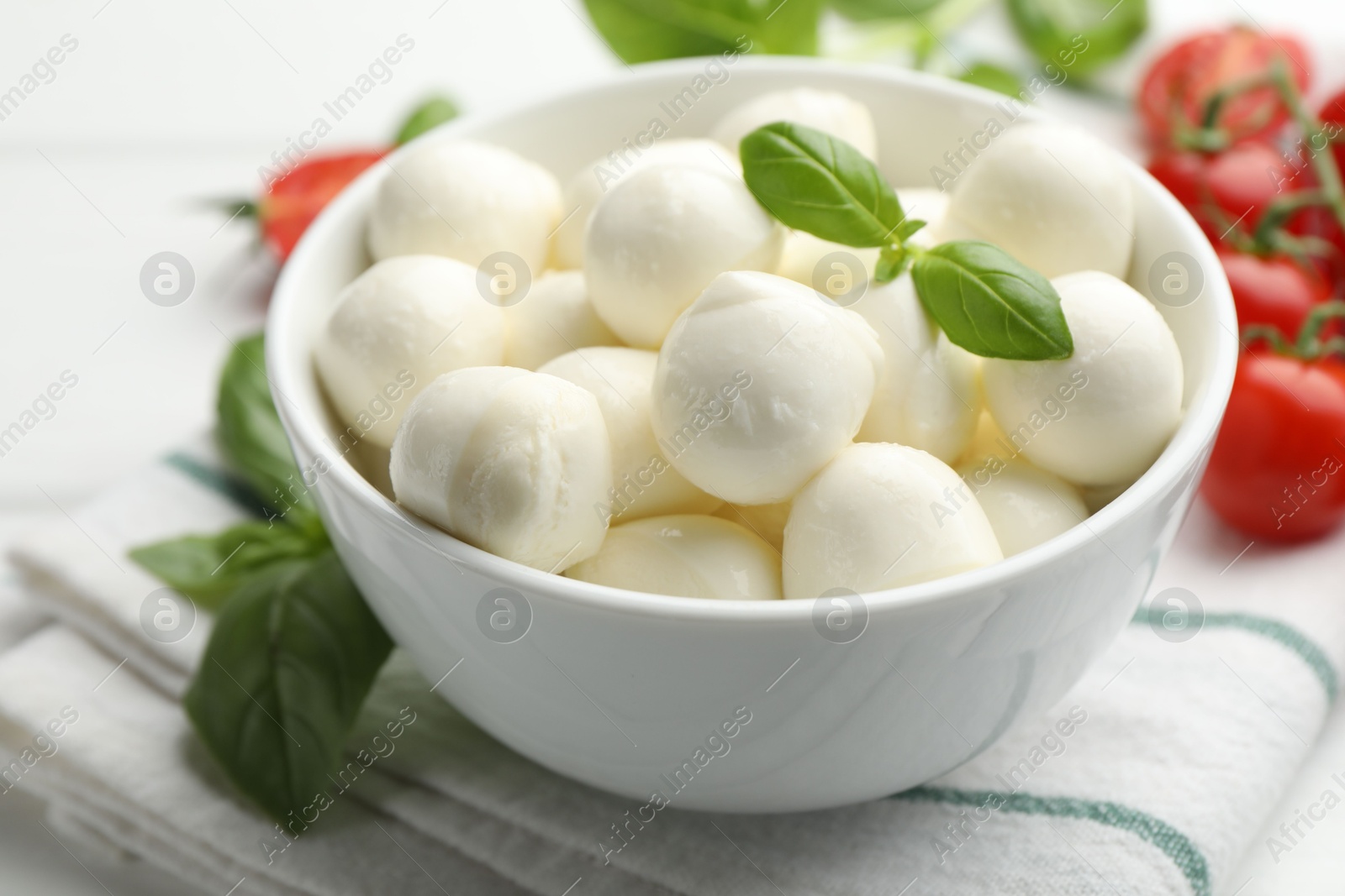 Tasty mozzarella cheese balls in bowl, basil and tomatoes on table, closeup Photo of Tasty mozzarella cheese balls in bowl, basil and tomatoes on table, closeup