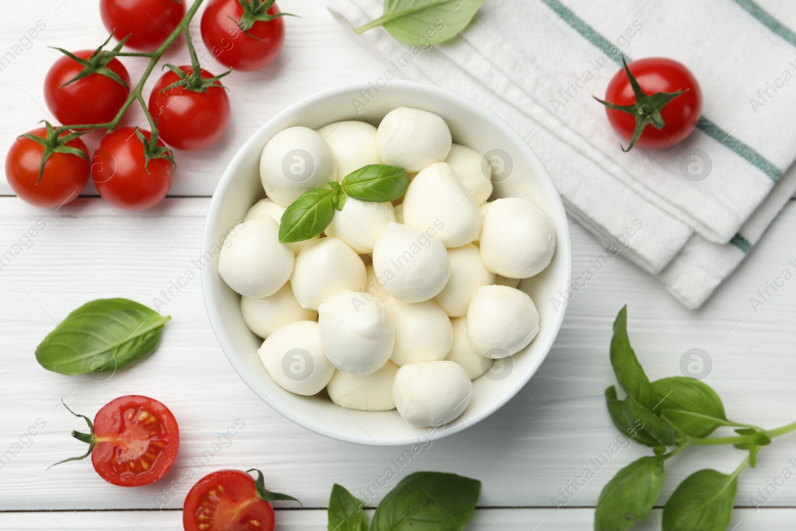 Tasty mozzarella cheese balls in bowl, basil and tomatoes on white wooden table, flat lay Photo of Tasty mozzarella cheese balls in bowl, basil and tomatoes on white wooden table, flat lay