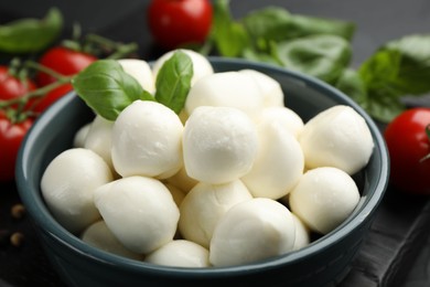 Photo of Tasty mozzarella cheese balls in bowl, basil and tomatoes on table, closeup