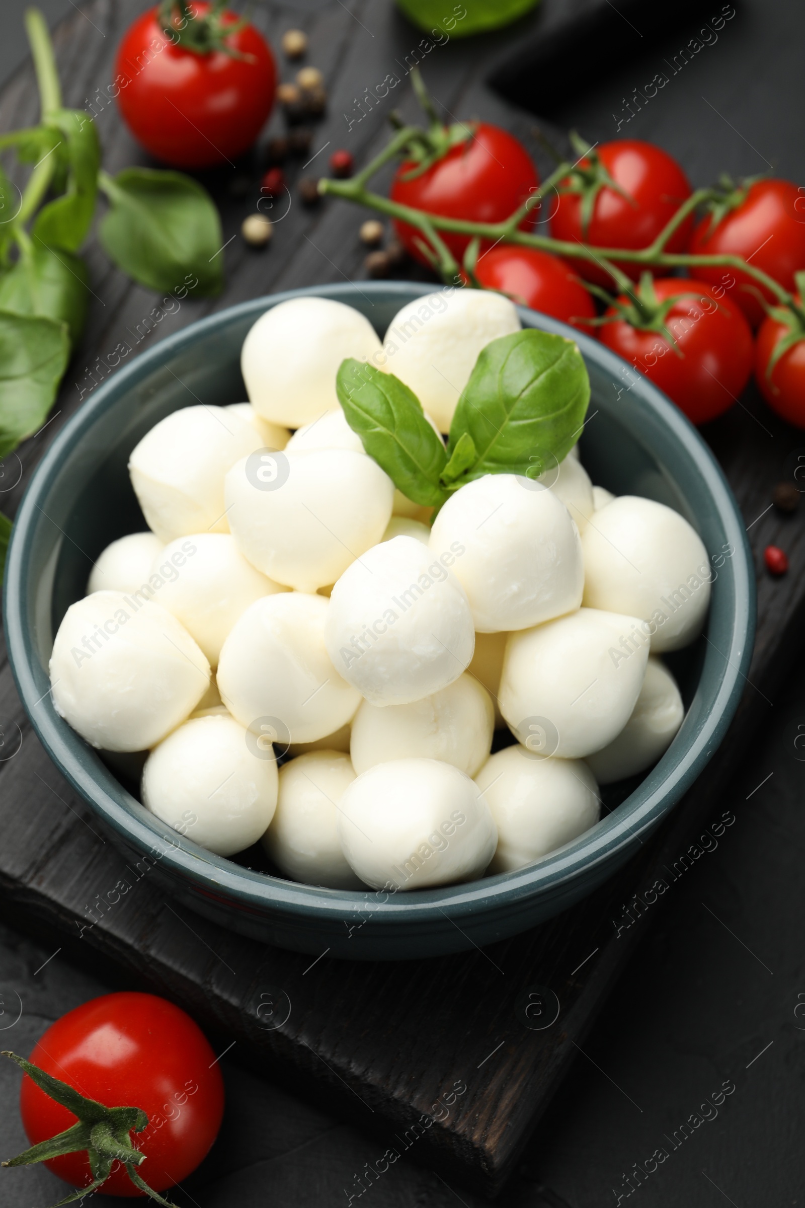 Tasty mozzarella cheese balls in bowl, basil, peppercorns and tomatoes on black table, above view Photo of Tasty mozzarella cheese balls in bowl, basil, peppercorns and tomatoes on black table, above view